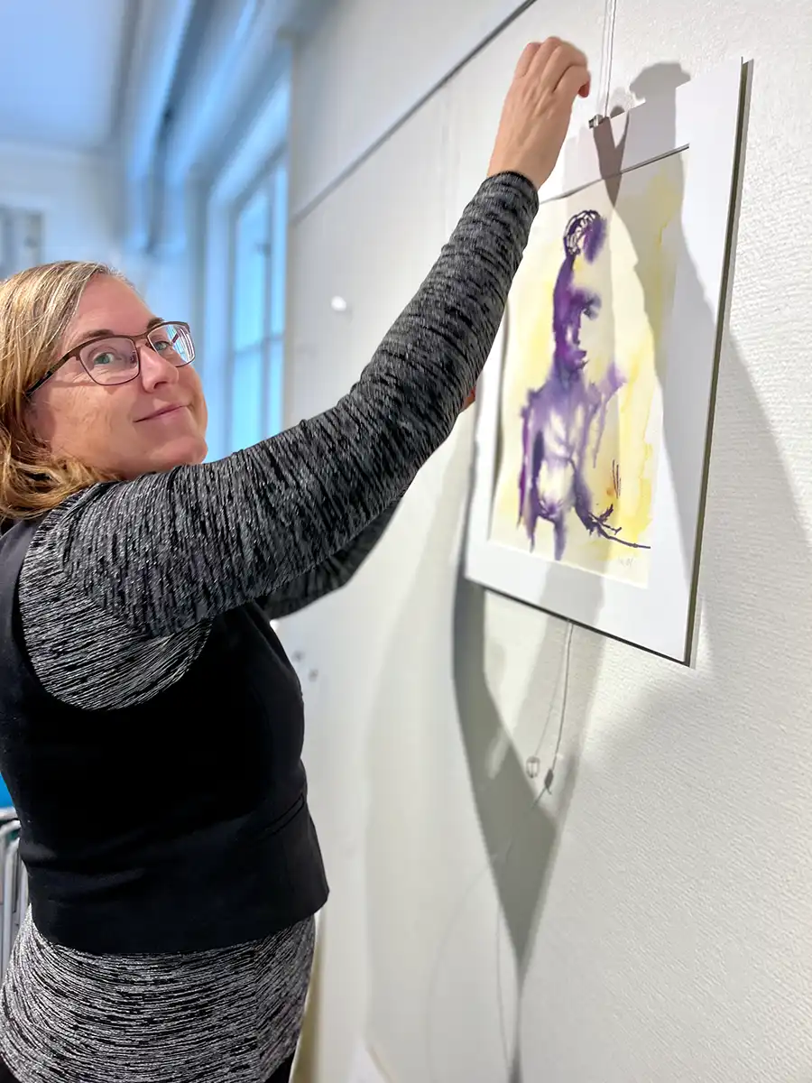 Helene Engström i ateljén i Norrköping. På fotot syns en suddig bild av Helene när hon med hjälp av en pendel formar ansiktet på lerfiguren. Fokuset i bilden ligger på lerfiguren hon arbetar med. Längst ner på skulpturens rygg står det Helene intryckt med hjälp av en stämpel.